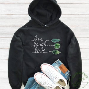 May include: Black hooded sweatshirt with the words "live laugh love" written in white cursive script. The words are accompanied by three green leaves.