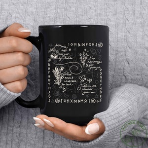 May include: Black coffee mug with white text and illustrations of various herbs, flowers, and symbols. The text includes phrases like "Always throw spilled salt over your left shoulder" and "Plant roses & lavender for luck".