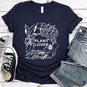 May include: A navy blue t-shirt with a white graphic of plants and a squirrel. The text "PLANT LOVER" is written on the shirt.