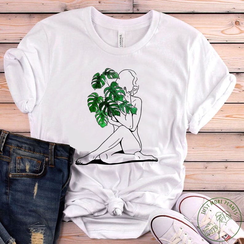 May include: White t-shirt featuring a line drawing of a person holding a green monstera plant. The text "Just More Plants" is printed on a white canvas shoe.