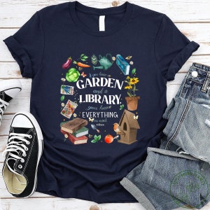 May include: A navy blue t-shirt with a watercolor illustration of a garden and a library. The text reads "If you have a GARDEN and a LIBRARY, you have EVERYTHING you need - Cicero".