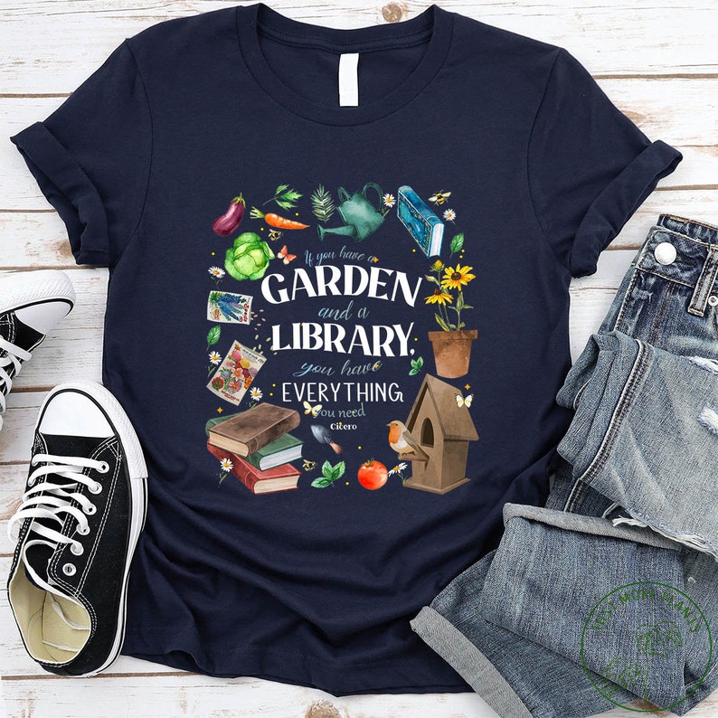 May include: A navy blue t-shirt with a watercolor illustration of a garden and a library. The text reads "If you have a GARDEN and a LIBRARY, you have EVERYTHING you need - Cicero".