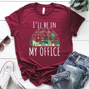 May include: A maroon t-shirt with the text "I'll be in my office" and a graphic of a greenhouse with plants.