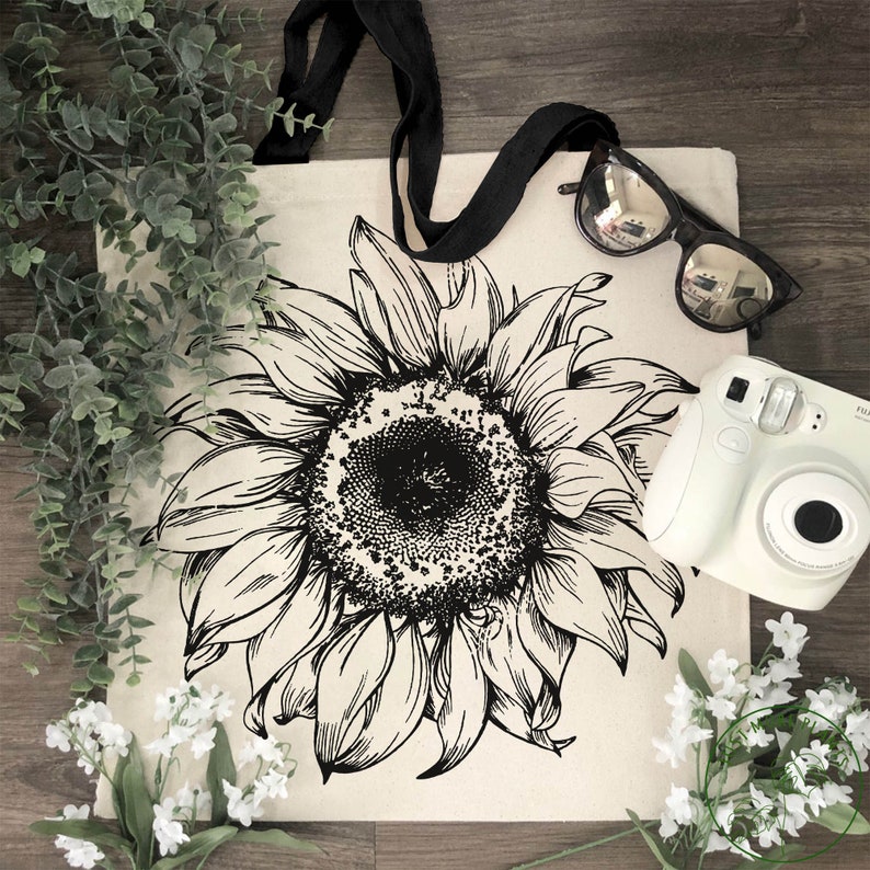 Peut inclure: Un sac fourre-tout noir et blanc avec un grand motif de tournesol. Le sac a des anses noires et est en toile.