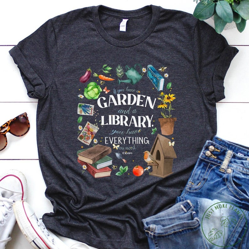 May include: A dark gray t-shirt with a graphic design featuring a garden and a library with the text "If you have a garden and a library, you have everything you need - Cicero".