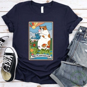 May include: A navy blue t-shirt with a cartoon cat holding a watering can in a garden setting. The text "THE PLANT KILLER" is below the cat.
