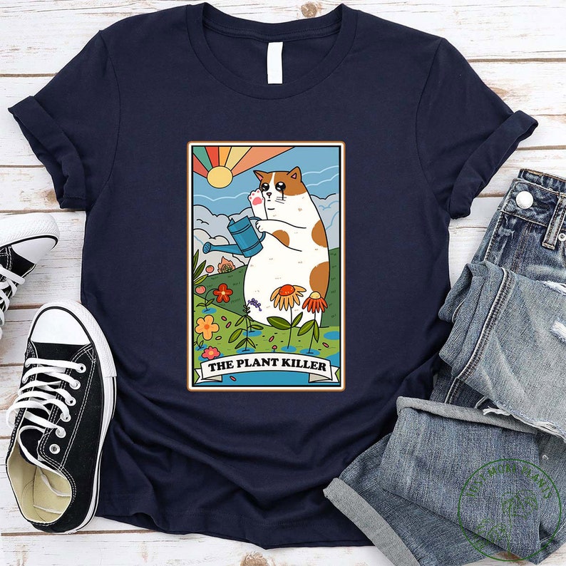 May include: A navy blue t-shirt with a cartoon cat holding a watering can in a garden setting. The text "THE PLANT KILLER" is below the cat.
