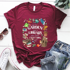 May include: A maroon t-shirt with a graphic design featuring a garden and a library with the text "If you have a GARDEN and a LIBRARY, you have EVERYTHING you need - Cicero".