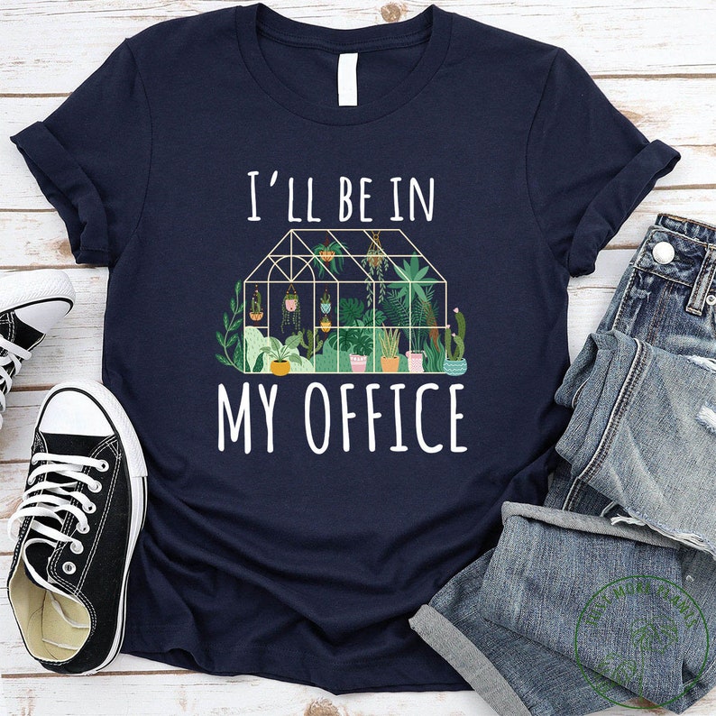 May include: A navy blue t-shirt with white text that reads "I'll be in my office". The text is above a graphic of a greenhouse filled with plants.