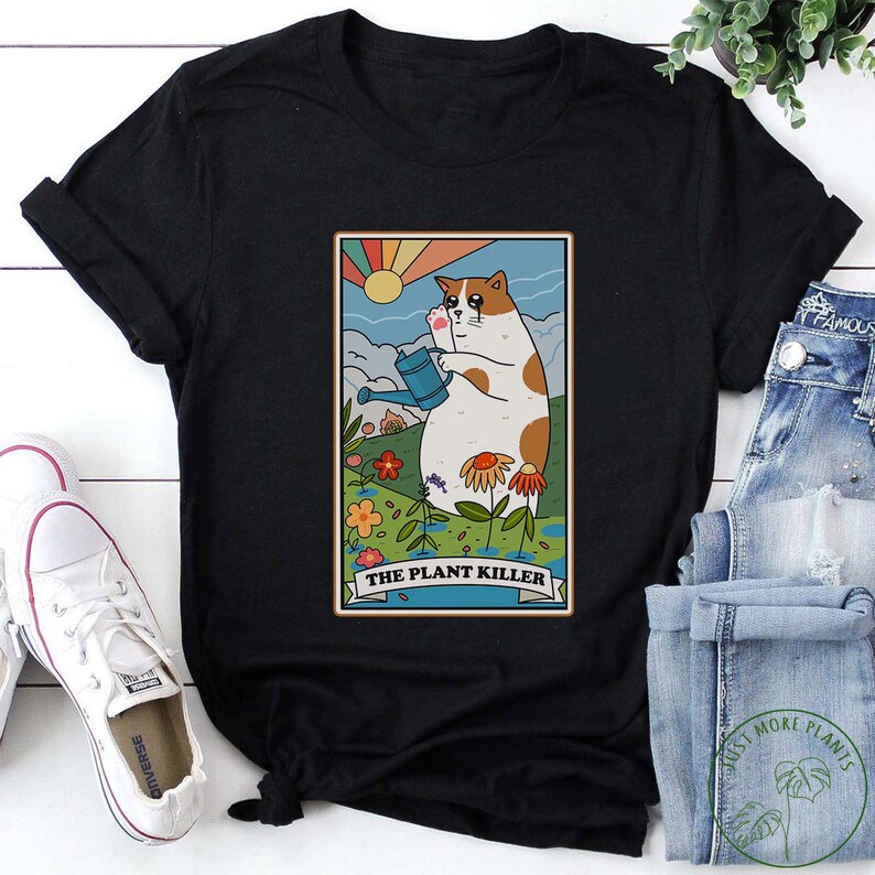 May include: Black t-shirt with a graphic of a cat holding a watering can in a garden with the text "The Plant Killer".
