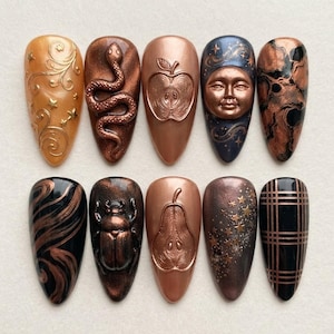 Peut inclure: Un ensemble de dix faux ongles en amande arborant des motifs en cuivre métallique et noir. Les designs incluent un serpent enroulé, un visage de lune, un scarabée, une pomme, une poire, des volutes dorées, des étoiles et un motif écossais.