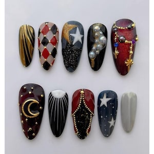 Peut inclure: Dix faux ongles aux designs variés. Les ongles présentent des couleurs or, rouge, noir et blanc, avec des motifs comprenant des rayures, des arlequins, des étoiles et des embellissements. Certains ongles ont des paillettes, des perles et des accents dorés.