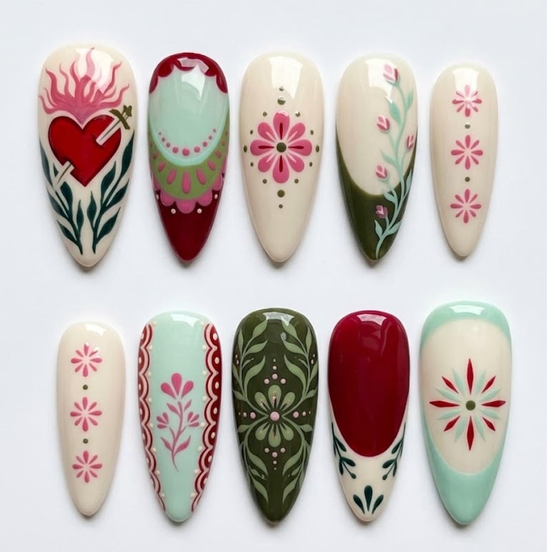 May include: A set of ten almond-shaped press-on nails featuring intricate hand-painted designs. The collection includes motifs such as a red sacred heart with a sword, floral patterns, geometric borders, and botanical vines in shades of cream, red, olive green, and mint.
