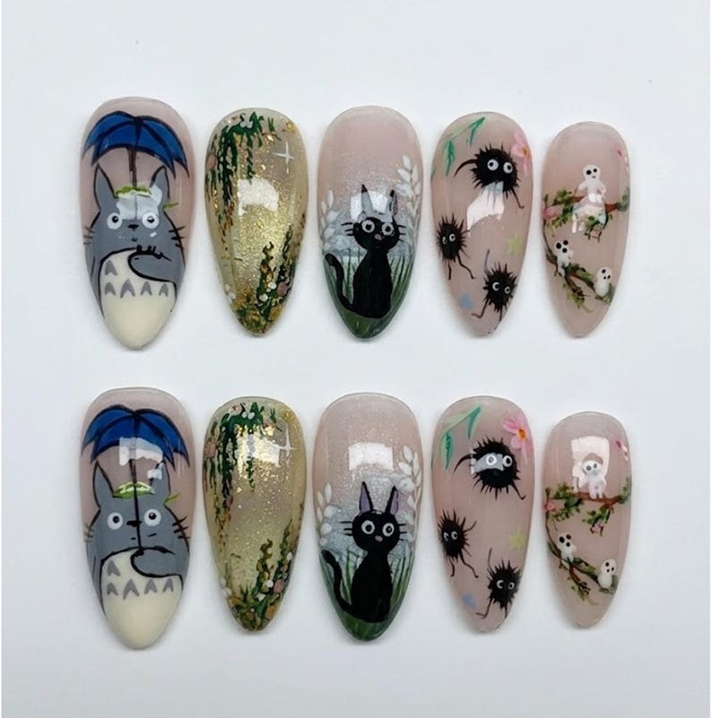Puede incluir: Juego de diez u&ntilde;as postizas en forma de almendra, cada una pintada a mano con un dise&ntilde;o diferente. Los dise&ntilde;os incluyen un personaje de dibujos animados gris bajo un paraguas azul, un gato negro y otras ilustraciones caprichosas sobre un fondo nude.