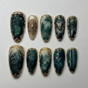 May include: A set of ten press-on nails featuring dark green and cream tones with intricate forest, mountain, bat, and cat illustrations. Each nail is accented with gold metallic filigree borders and one nail features a central gold oval emblem.