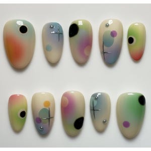 May include: A set of ten artificial nails with a rounded shape. Each nail features a unique design with gradients of color, including pink, orange, green, and blue, along with black circles, silver accents, and geometric shapes.