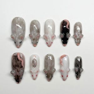 May include: A set of ten press-on nails featuring hand-painted mouse designs in various colors including white, gray, brown, and black. Each nail displays a detailed mouse figure with small ears, eyes, and tails, showcasing a glossy finish.