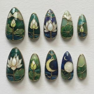 May include: A collection of ten almond-shaped nail art designs. Each nail showcases a unique design featuring a lotus flower, moon, or water lily in green, blue, white, and gold. The designs are detailed and intricate, with a stained-glass effect.