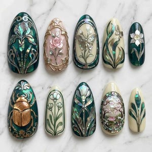 Peut inclure: Dix faux ongles ornés de motifs uniques. Chaque ongle présente des œuvres d'art détaillées, notamment des motifs floraux, un papillon et un scarabée, avec des accents irisés et métalliques. Les ongles sont de formes et de couleurs variées.