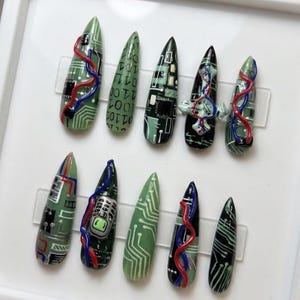 May include: A set of ten stiletto-shaped press-on nails featuring a tech-inspired theme. The designs include green and black circuit board patterns, binary code, a miniature mobile phone graphic, and raised red and blue 3D gel accents.