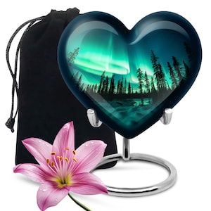 Puede incluir: Un recuerdo de vidrio en forma de corazón con una foto de la aurora boreal sobre un bosque. El recuerdo está en un soporte plateado y viene con una bolsa de terciopelo negro.