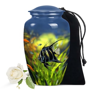 May include: Blue ceramic urn featuring a black and white angelfish swimming in a green and yellow underwater scene. The urn has a lid and comes with a black velvet drawstring bag.