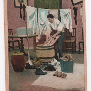 Peut inclure: Carte postale vintage montrant un homme faisant la lessive dans un tonneau en bois. Des vêtements blancs sont suspendus à une corde à linge. Le texte en bas dit : "Un jeune homme souhaite faire la connaissance d'une jeune femme, l'argent et l'apparence ne comptent pas (en vue du mariage)."