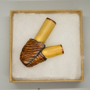May include: A wooden pipe with a brown and black patterned bowl and two yellow stems. The pipe is in a white box with a brown lid.