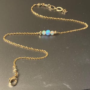 May include: A delicate gold chain necklace with three iridescent opal beads. The chain is a simple, fine chain with a lobster clasp.