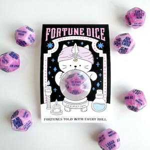 Può includere: Un set di dadi a 20 facce rosa marmorizzato con testo blu, confezionato su un cartoncino bianco e nero raffigurante un gatto con turbante e una sfera di cristallo. Il cartoncino riporta FORTUNE DICE e FORTUNES TOLD WITH EVERY ROLL, con candele e boccette.