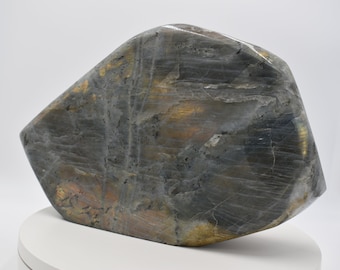 May include: A large, gray, iridescent labradorite stone with gold and copper hues. The stone is shaped like a teardrop and has a smooth, polished surface.