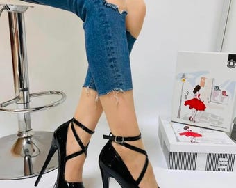 Könnte beinhalten: Schwarze Plateauschuhe mit einem Kreuzriemen-Design und einem Schnallenverschluss. Die Absätze sind sehr hoch und haben eine dicke Plattform.