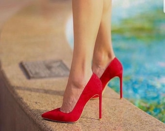 Puede incluir: Un par de tacones altos de gamuza roja con punta puntiaguda y tacón de aguja.