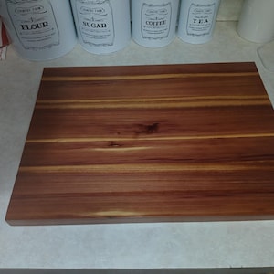May include: A rectangular wooden cutting board with a rich, reddish-brown color and visible wood grain. The board is made of solid wood and appears to be new. It is a kitchen item, suitable for food preparation.