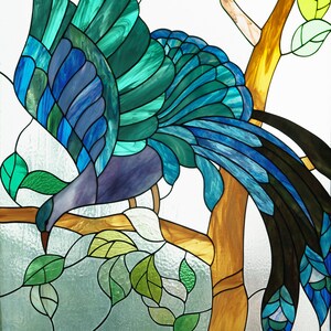 May include: Stained glass artwork featuring a bird with teal, blue, and purple plumage perched on a tree branch. The bird is surrounded by green leaves and a brown tree trunk, with a white background.