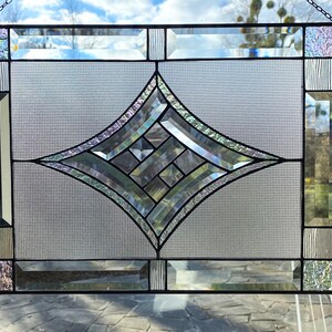 以下が含まれることがあります： 幾何学的なダイヤモンドデザインが中央にあるステンドグラスの窓パネル。 パネルは、黒い金属フレームを備えた透明で虹色のガラスが特徴です。 窓は長方形で、中央にグリッドパターンがあります。