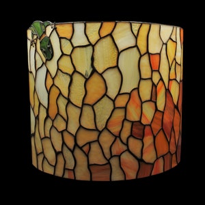 May include: A cylindrical stained glass lamp shade with a mosaic pattern in shades of yellow, orange, and brown. A green frog is perched on the rim. The lamp shade is likely for a table lamp or floor lamp.