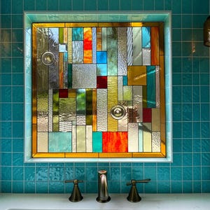 May include: A colorful stained glass window with a geometric design. The window features a variety of shapes and colors, including red, orange, yellow, blue, and green. The window is set in a white frame and surrounded by teal tiles.