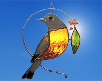 May include: A stained glass bird with a gray head, orange and red chest, and green leaves with orange berries. The bird is hanging from a metal ring.