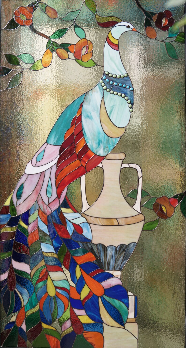 May include: Stained glass panel featuring a colorful peacock perched on a vase. The peacock has a white head, turquoise body, and a vibrant tail with red, orange, blue, and green feathers. The background is a textured, golden-green.