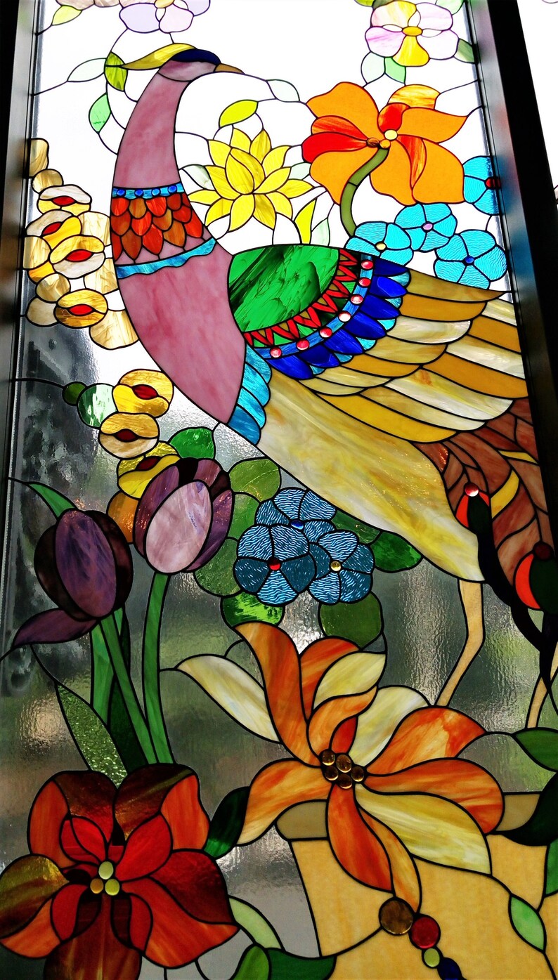 May include: Stained glass panel featuring a colorful peacock and floral design. The peacock has a pink head, green back, and yellow and brown feathers. Flowers include orange, yellow, and blue blooms. The artwork is framed with black borders.
