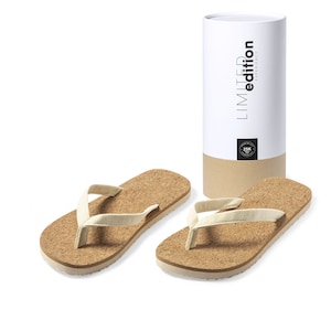 Puede incluir: Dos pares de chanclas de corcho con una tira de lona beige claro. Las chanclas están empaquetadas en un tubo de cartón con el texto "LIMITED edition EXPERIENCE" impreso en el lateral.