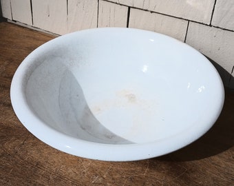 May include: A white ceramic bowl with a slightly textured surface. The bowl is empty and has a slight discoloration on the bottom.