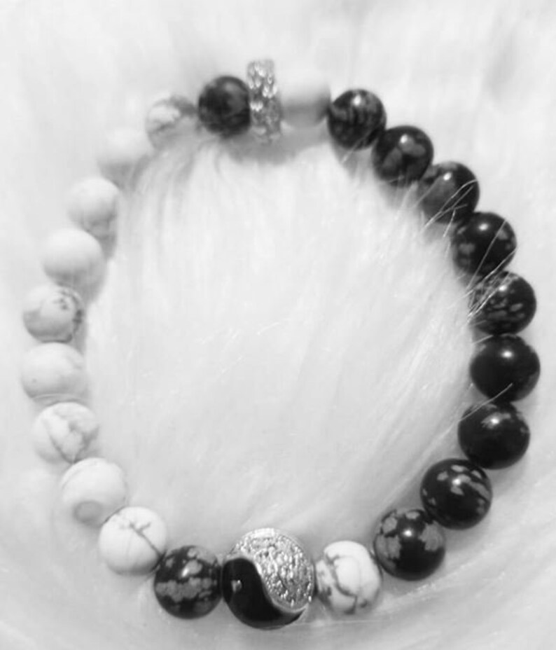 Puede incluir: Un brazalete de cuentas yin yang en blanco y negro con piedras blancas y negras. El brazalete tiene un cierre plateado.