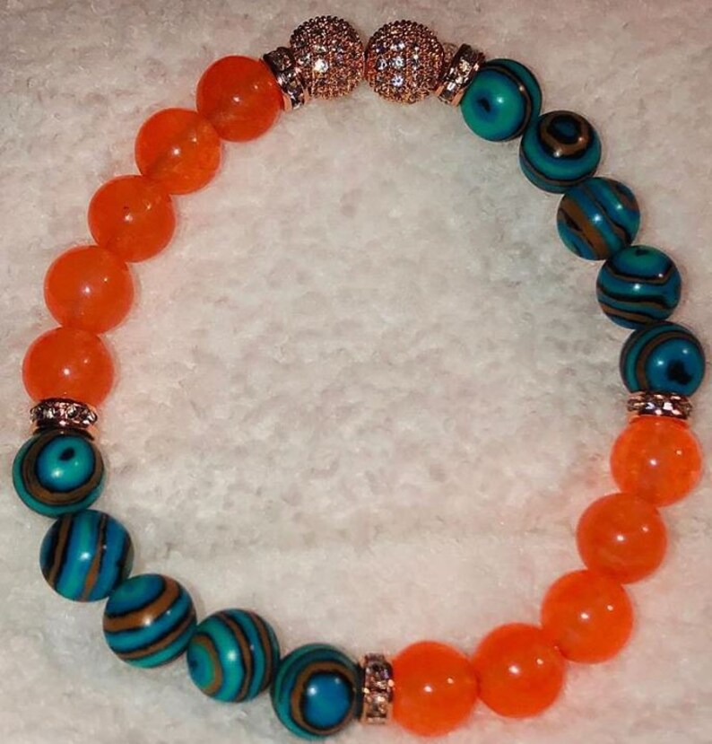 Puede incluir: Un brazalete con cuentas naranjas y azules. Las cuentas est&aacute;n separadas por separadores dorados con diamantes de imitaci&oacute;n transparentes. El brazalete est&aacute; hecho con un cord&oacute;n el&aacute;stico.