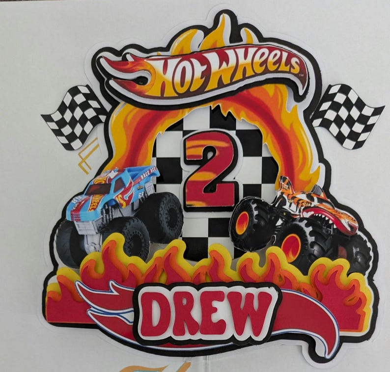 May include: A colorful Hot Wheels cake topper featuring two monster trucks, flames, and the name "DREW." The number "2" is prominently displayed, with checkered flags on either side. The Hot Wheels logo is at the top.