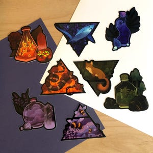 May include: A collection of colorful stickers featuring various designs. The stickers include a shark, a fox, a snake, bees, and potion bottles. Each sticker is set within a triangular frame, with a white and blue background.