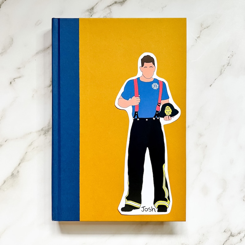 May include: A hardcover book with a mustard yellow cover and a blue spine. A sticker of a firefighter in a blue shirt, black pants, and red suspenders is on the cover. The firefighter is holding a helmet. The name "Josh" is at the bottom.