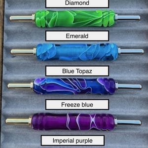 May include: A collection of colorful pen holders with various designs and names. The colors include yellow, white, green, blue, purple, and red. Each pen holder has a silver tip and a label with its name, such as "Canary" and "Diamond."