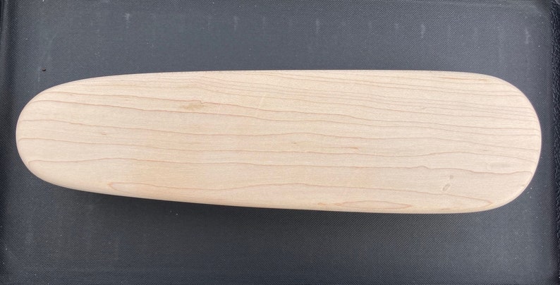 May include: A smooth, oval-shaped wooden cutting board made of maple wood.